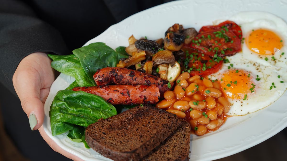 A delicious breakfast plate featuring eggs, sausages, beans, toast, and fresh vegetables.